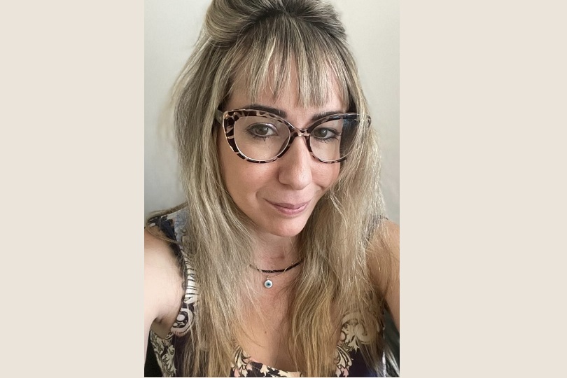 Renata é uma mulher de 38 anos. Ela tem a pele clara e longos cabelos loiros, com mechas castanhas. Ela usa óculos tigrados, blusa bege e sorri para a câmera.