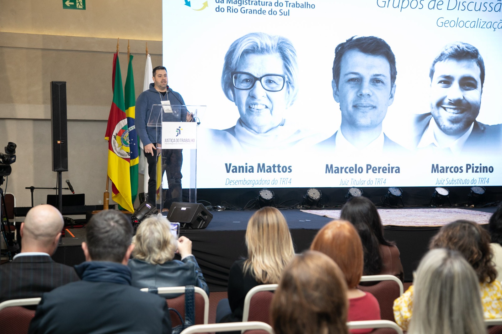 Juiz Marcos Pizino apresentando as conclusões do seu público. Aparece parte do público na frente do palco.