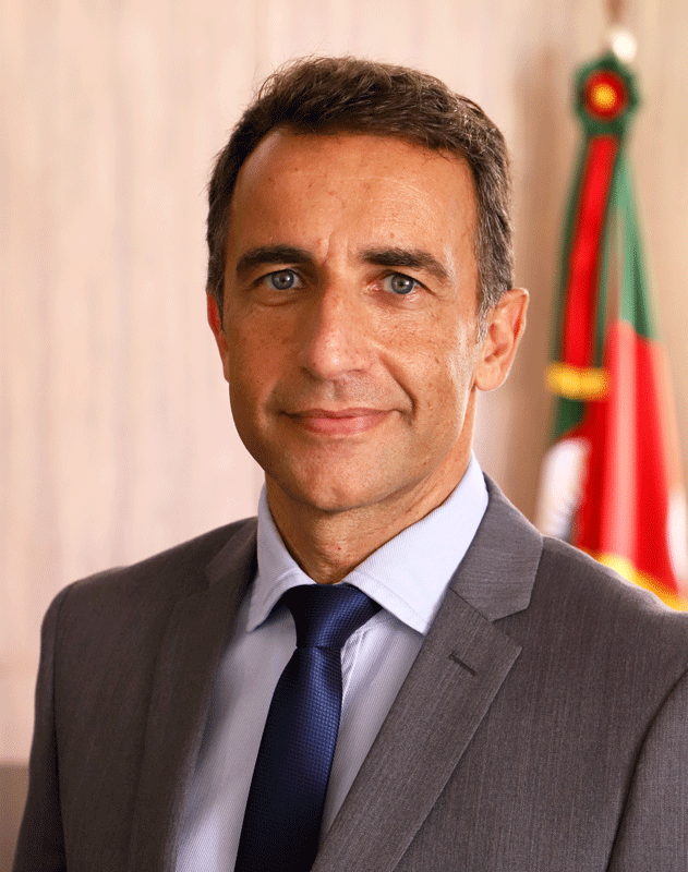 Retrato do servidor André Farias. Ele tem a pele e os olhos claros, e o cabelo castanho claro e curto. Veste terno cinza, camisa azul claro e gravara azul escuro.