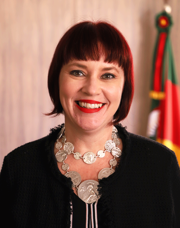 Retrato da servidor Barbara Casaletti. Ela tem a pele clara e os olhos castanhos. Seu cabelo tem um tom de ruivo escuro, é curto, cortado na linha do queixo, e tem uma franja reta cortada pouco acima das sobrancelhas. Está maquiada com um batom vermelho. Usa casaco e blusa pretos e um colar formado por medalhas prateadas com imagens de santos.