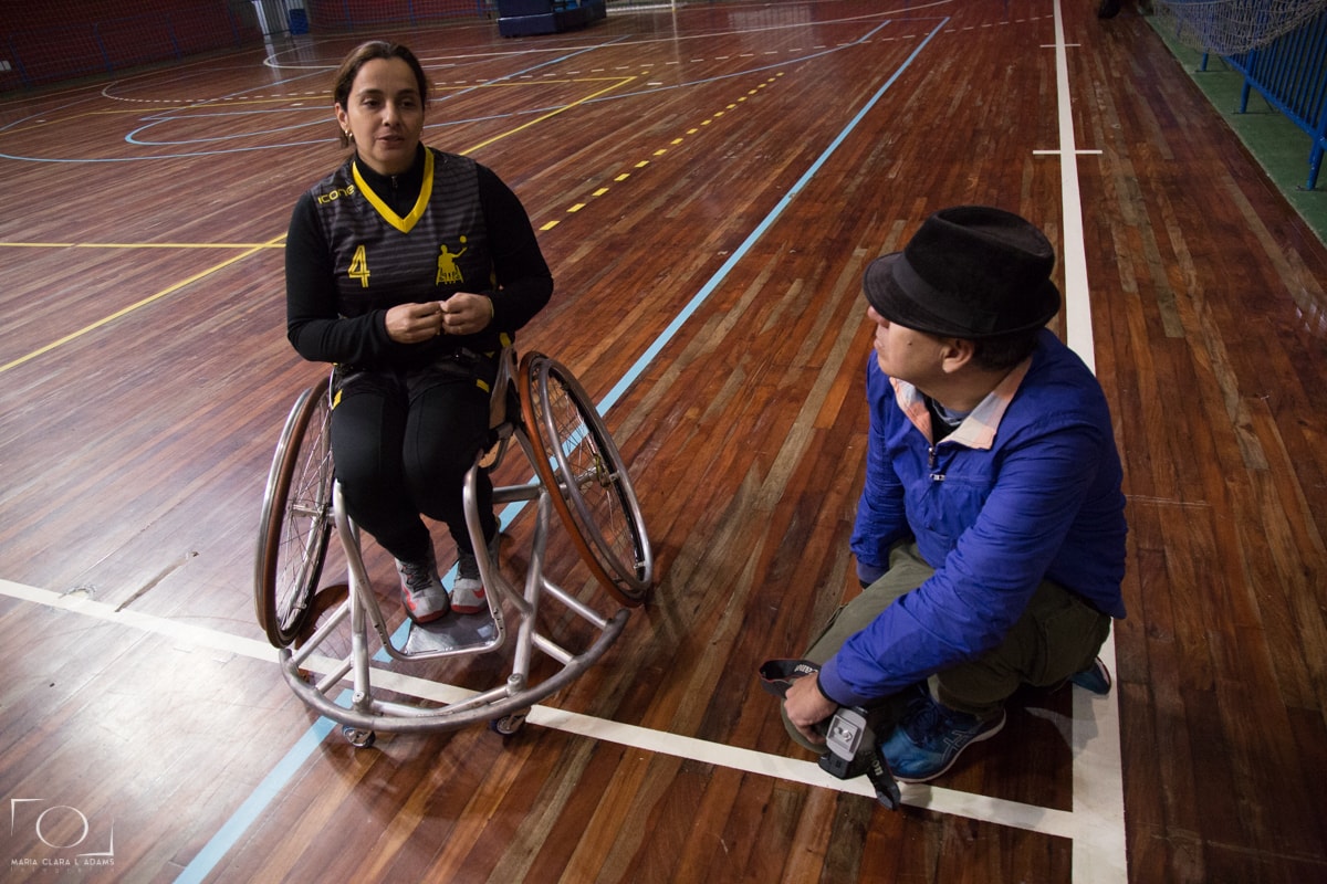 Cíntia, na cadeira de rodas, explica como funciona o jogo de basquete para Caio.