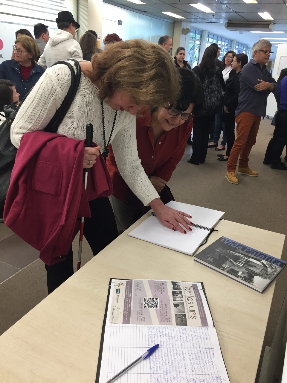 Elaine lendo o livro de descrições das fotos em Braille durante a abertura da exposição Tantos Uns