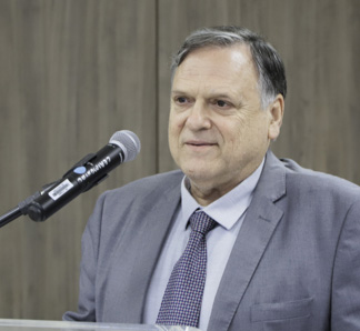 Homem branco grisalho vestindo traje formal cinza fala ao microfone