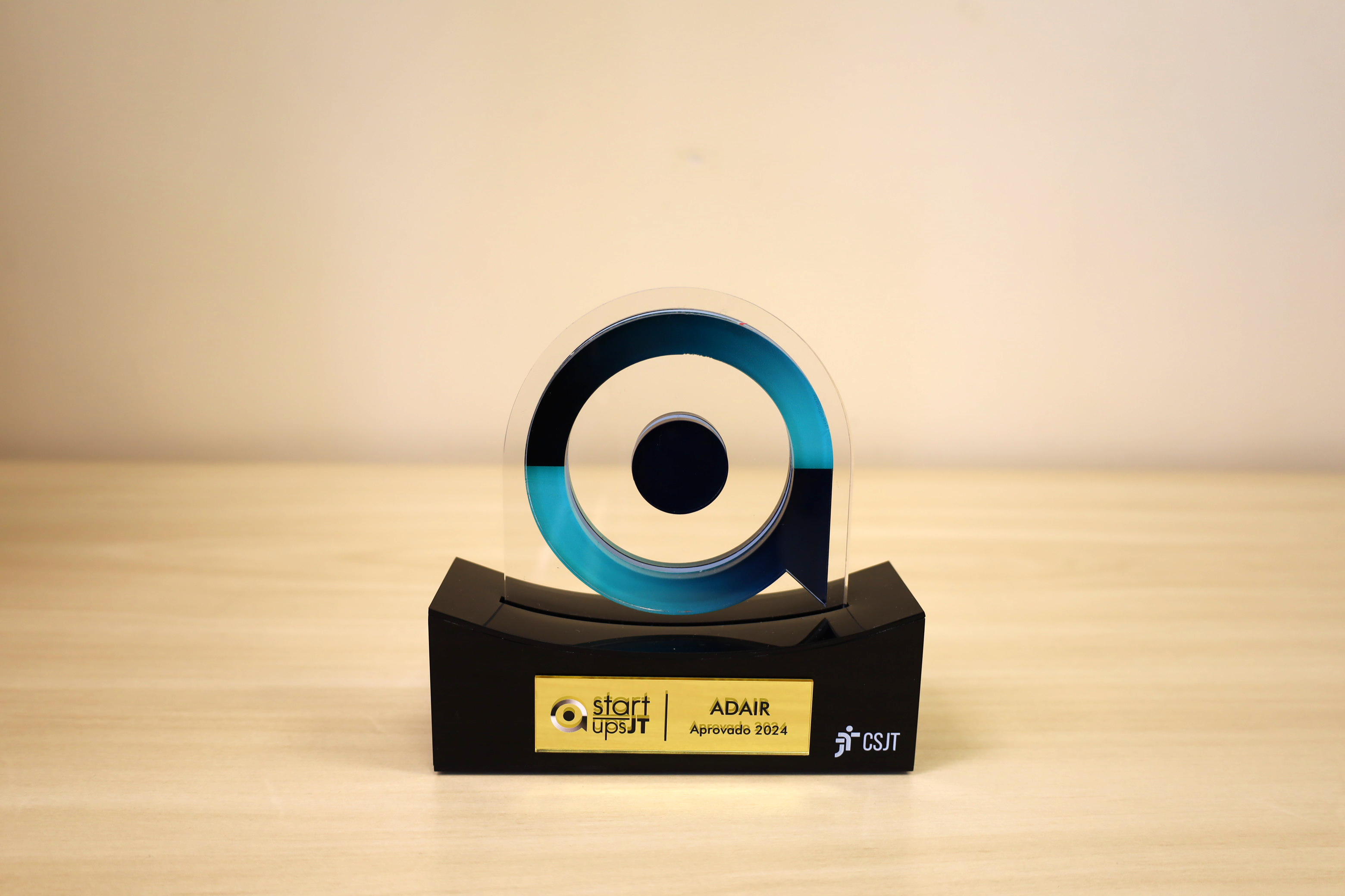 foto de troféu em acrilíco com logo em formato circular e círculo menor dentro, em base preta