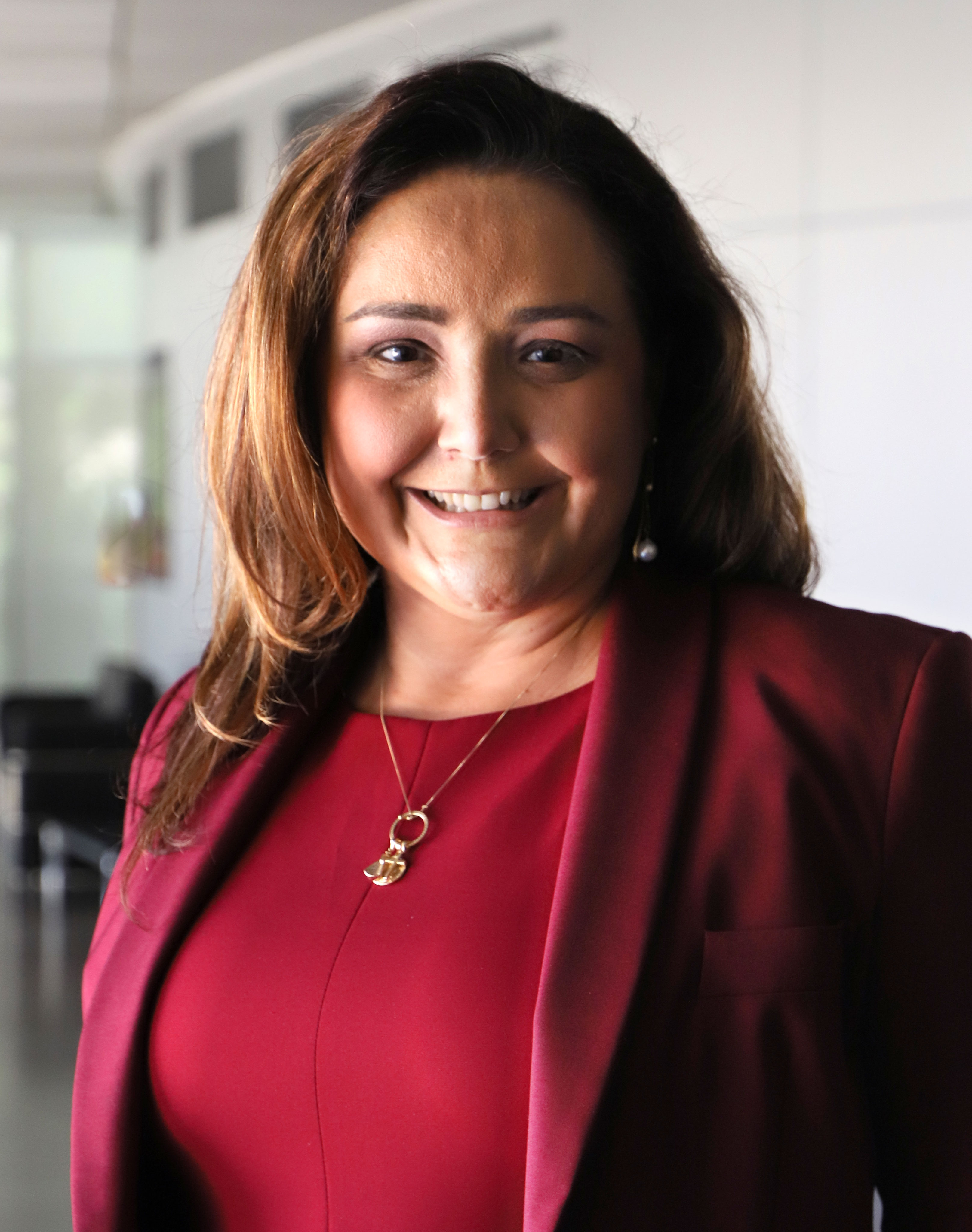 Maria Cristina é branca e de cabelo castanho liso. Sorri olhando para a foto.